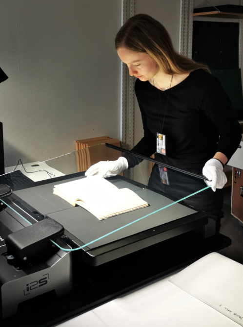 En person som står ved en stor scanner og svanner et dokument. Foto. 