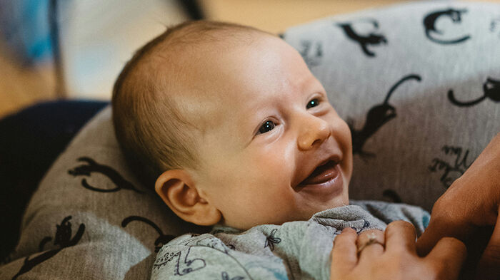En baby som smiler, voksne hender kilder den på magen. Foto.