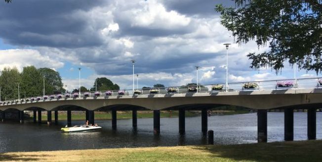 En bro over et vann, en båt på vannet er på vei inn under broen. Fotografi.