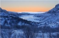 Vinterlandskap med utsyn nedover en dal med fjord og fjell. Foto.