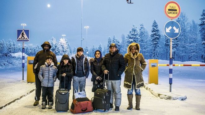 Seven people standing in a road. Men, women and children with bags. Wintertime.