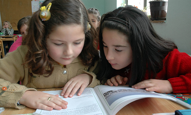Two girls reading a book together.