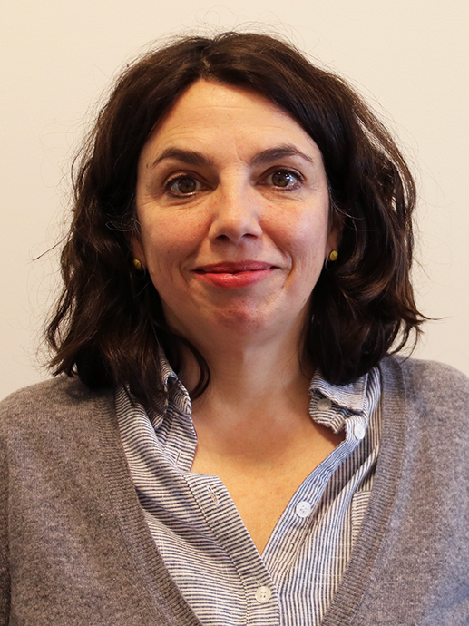 Portrait of Cristina Gomez-Baggethun. Dark-haired smiling woman, wearing white shirt and grey jacket. 