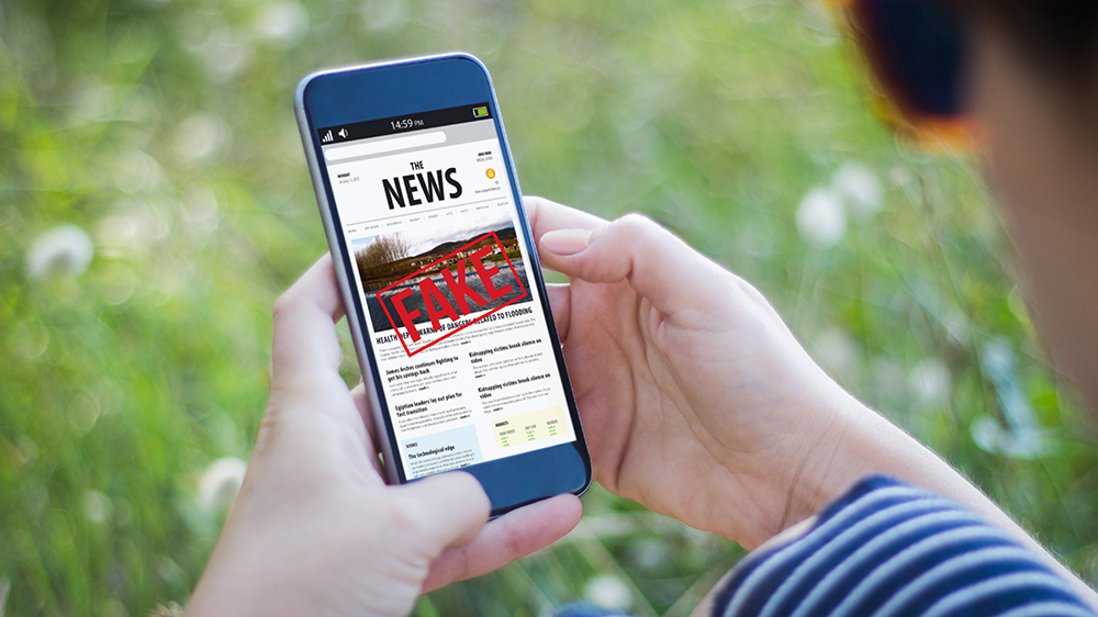Hands holding a smartphone with the words "news" and "fake" on the screen.