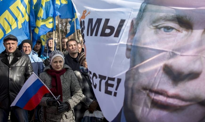 Folk protesterer mot Putin. En dame holder et russisk flagg, og et banner av Putin med slagord mot ham flyr i vinden.
