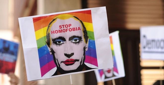 Et bilde av Putins ansikt med sminke, med regnbueflagg i bakgrunnen, med teksten "Stop Homofobia" i pannen hans.
