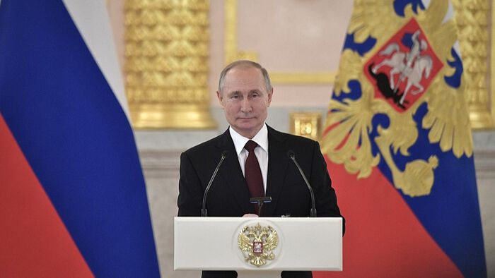 Putin står foran en talerstol med to store russiske flagg bak seg. Foto