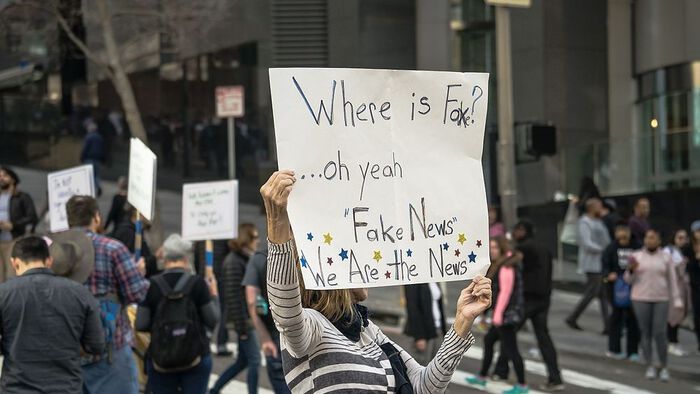 Flere mennesker som protesterer i gatene. Midt i bildet holder en kvinne opp en plakat som sier "Where is Fox.? ... Oh yeah. Fake News. We are the fake news". Foto