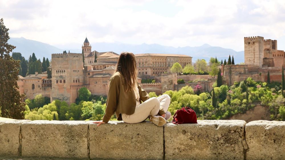 Kvinne sitter på en mur og ser på utsikten over eldre bygninger.