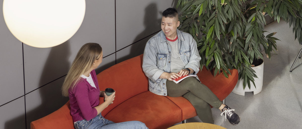 To studenter som sitter i en rød sofa og prater. Foto.