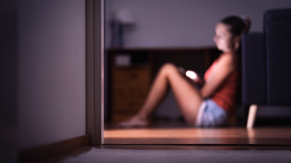 Ung kvinne sitter på gulvet med telefonen i hånda, lett ute av fokus.