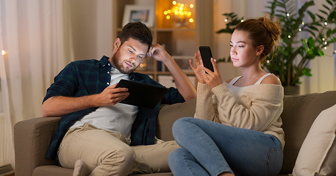 Man and woman sitting on sofa, each holding a smartphone