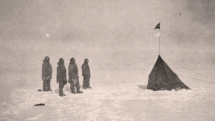 Old photo of four men dressed in winter clothes looking at a flag.