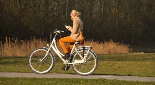Kvinne sykler mens hun leser på mobilen.