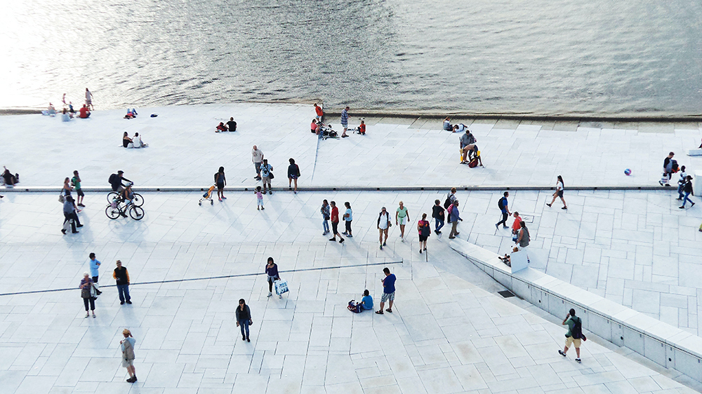 Bilde tatt ovenfra som viser mennesker på et hvitt gulv like ved vannet. Fra operaen i Oslo.