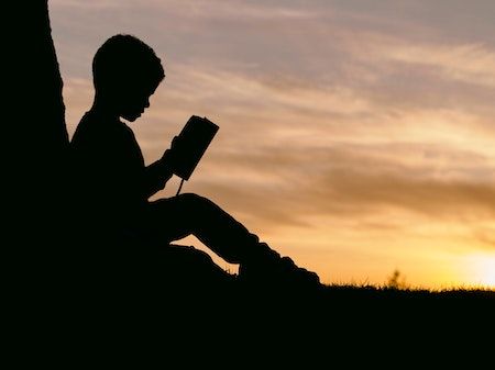 Barn sitter og leser i solnedgangen