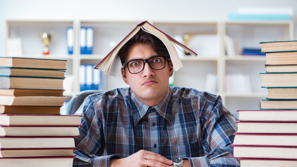 Foto av en gutt med et frustrert ansiktsuttrykk som er omringet av bøker med en bok på hodet.