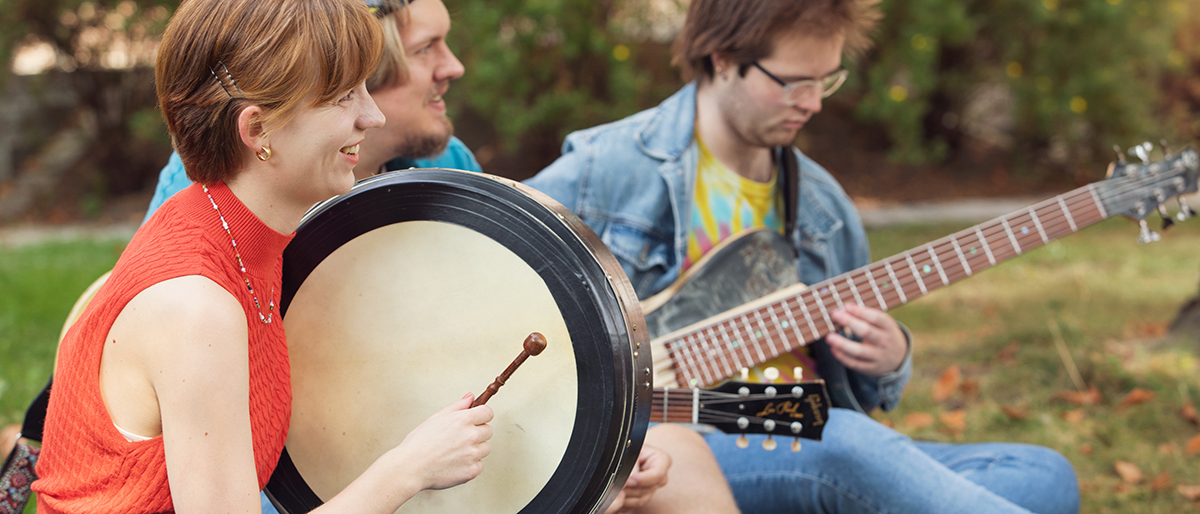 Group of students playing instruments while sitting on the lawn outside of the ZEB-building. Photo.