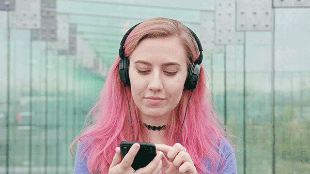 Kvinne med rosa hår og hodetelefoner trykker på smarttelefon.
