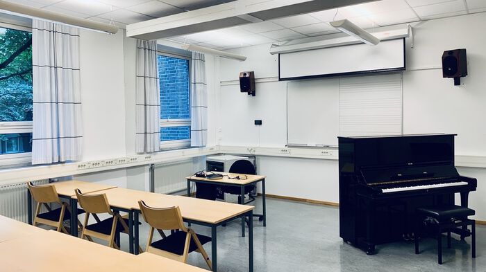 Overview of seminar room, tables, chairs and a piano.