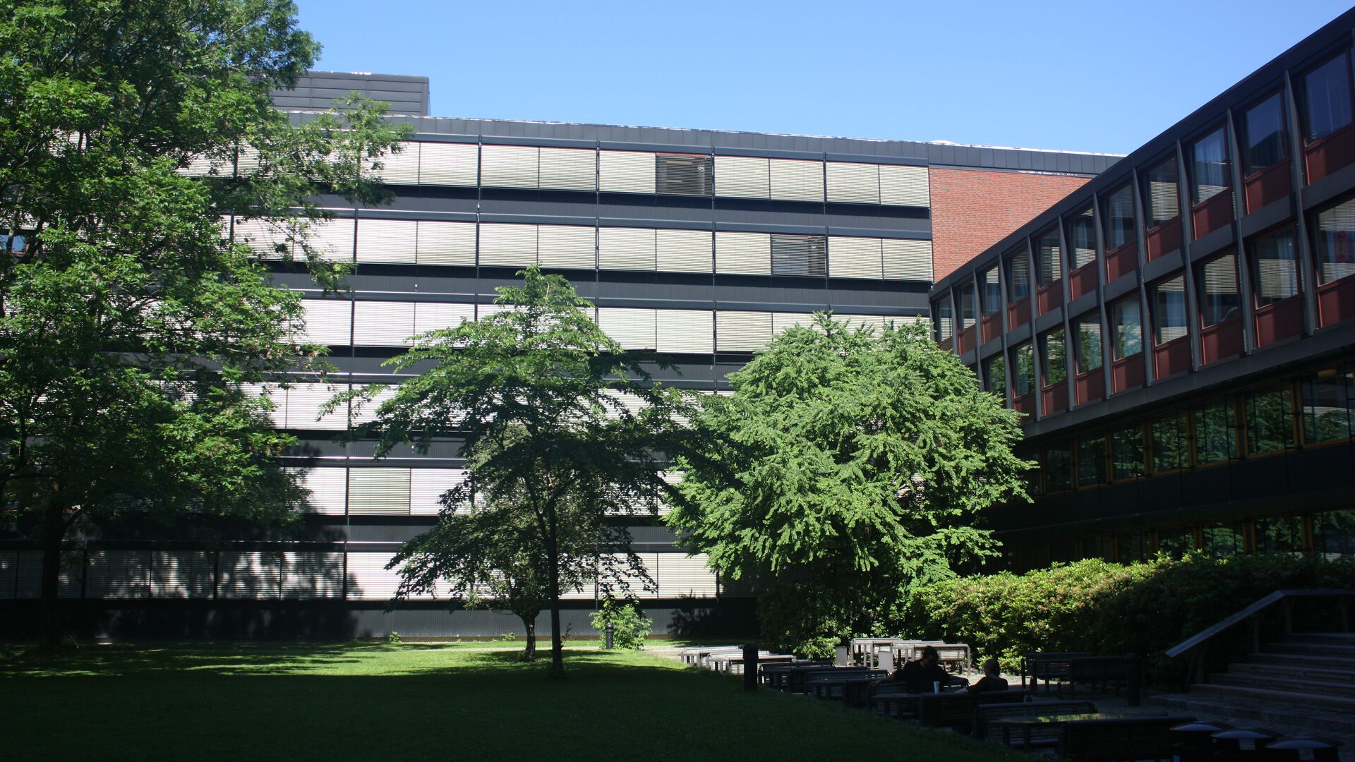 Office building in brick with six floors. Green trees and lawn in the foreground.