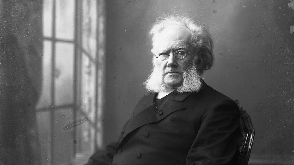 Black and white portrait of Henrik Ibsen. Old man with white hair and beard, small glasses, black suit.