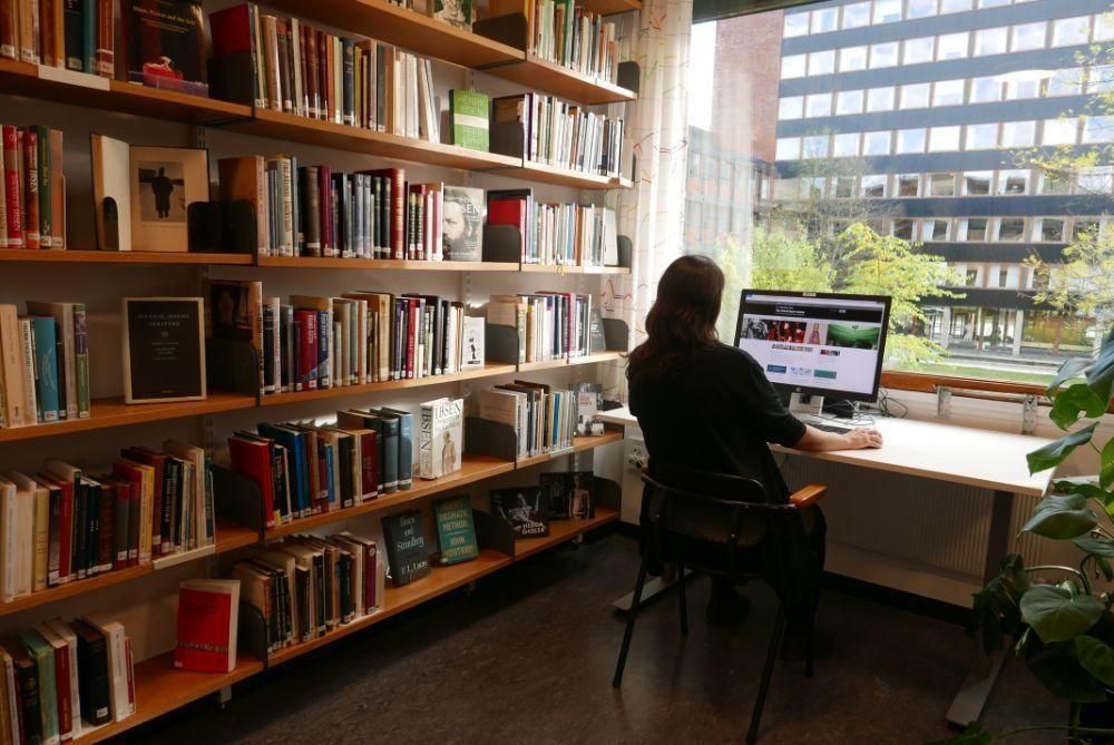 A person working at a computer next to a large bookshelf.