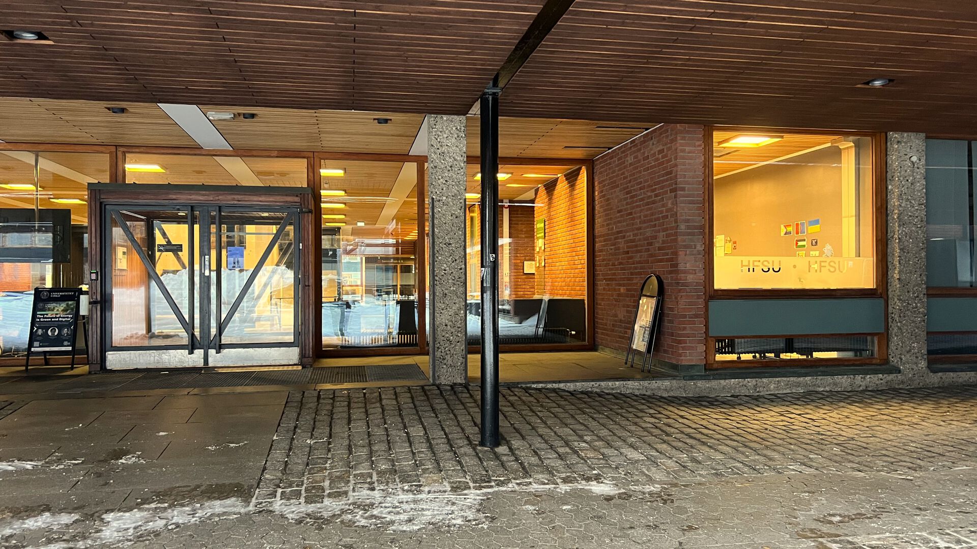 Inngangsparti til murbygning med store dører overbygget med tretak. Rester etter snø på bakken. 