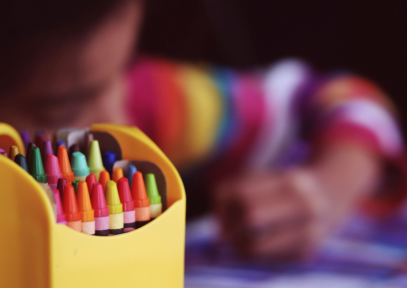 Colorful crayons; child drawing in the background