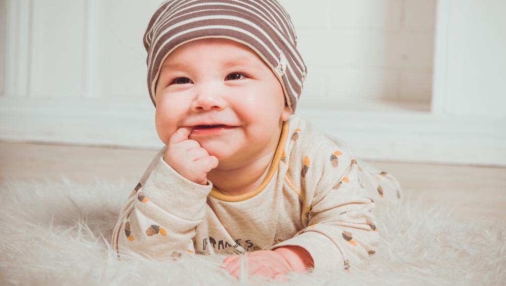 En baby som ligger på magen og smiler på et saueskinn på gulvet. Foto.