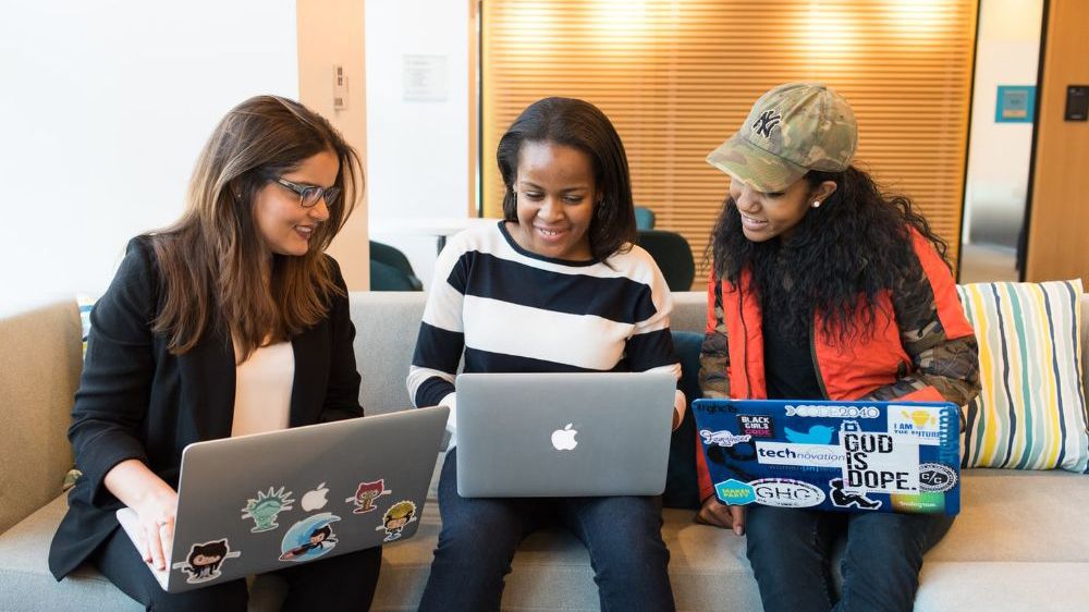 Three girls sitting and working together on their laptops. Photo.