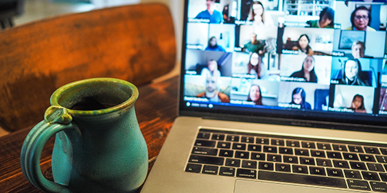 Fotografi av en laptop med bilder fra et web-møte, en blå kaffekopp i forgrunnen.