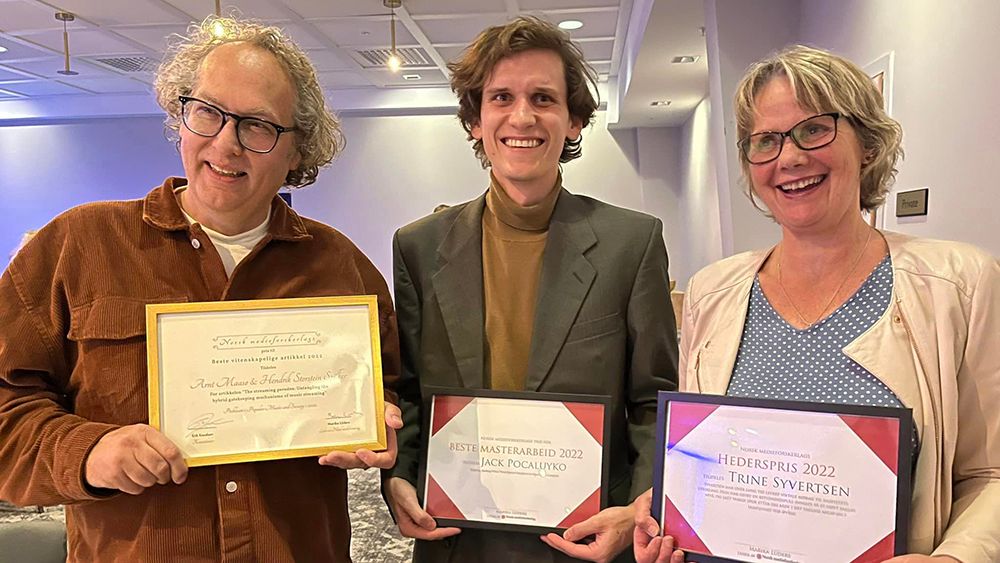 En mann, en yngre mann og en kvinne smiler og holder diplomer.