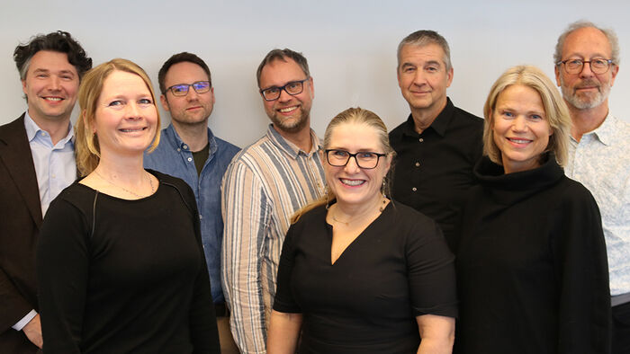 Gruppebilde av 8 personer i halvfigur, smilende.