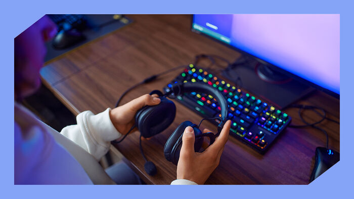 Foto av en gutt som holder øreklokker med en skjerm og fargerikt tastatur i bakgrunnen.