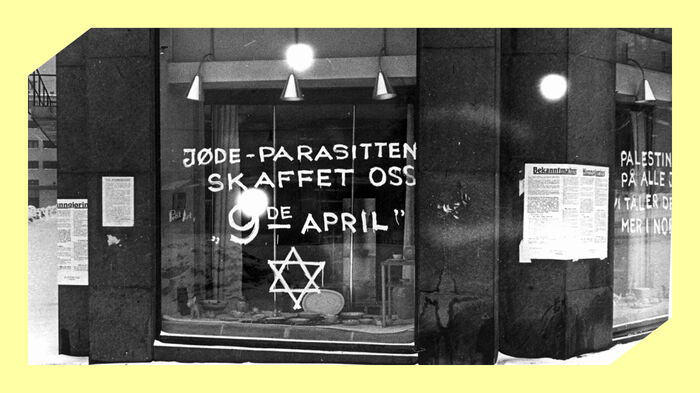 Et butikkvindu der det er er skrevet med hvit maling "Jøde-parasitten skafftet oss 9de april" og davidsstjernen. Svart/hvitt foto.