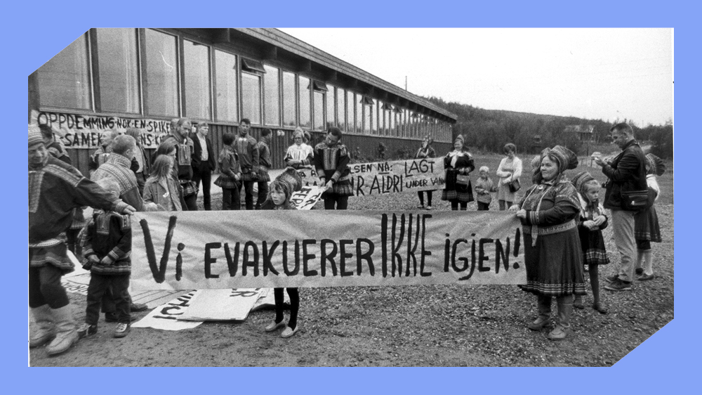 Svarthvit foto av kvinner, menn og barn i samisk drakt med bannere der det står "Vi evakuerer ikke igjen!".