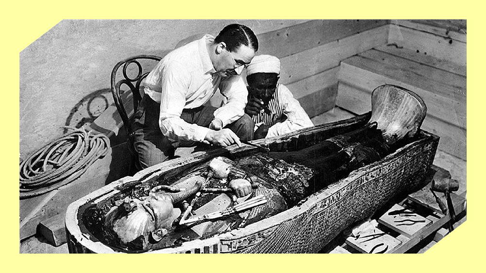 To menn sitter bøyd over en egyptisk mumie og studerer den nøye. Foto. 