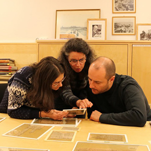 Tre personer ser på gamle papyrusbiter ved et bord.