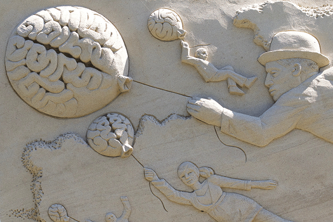 Sandskulptur av mennesker som holder ballonger formet som hjerner