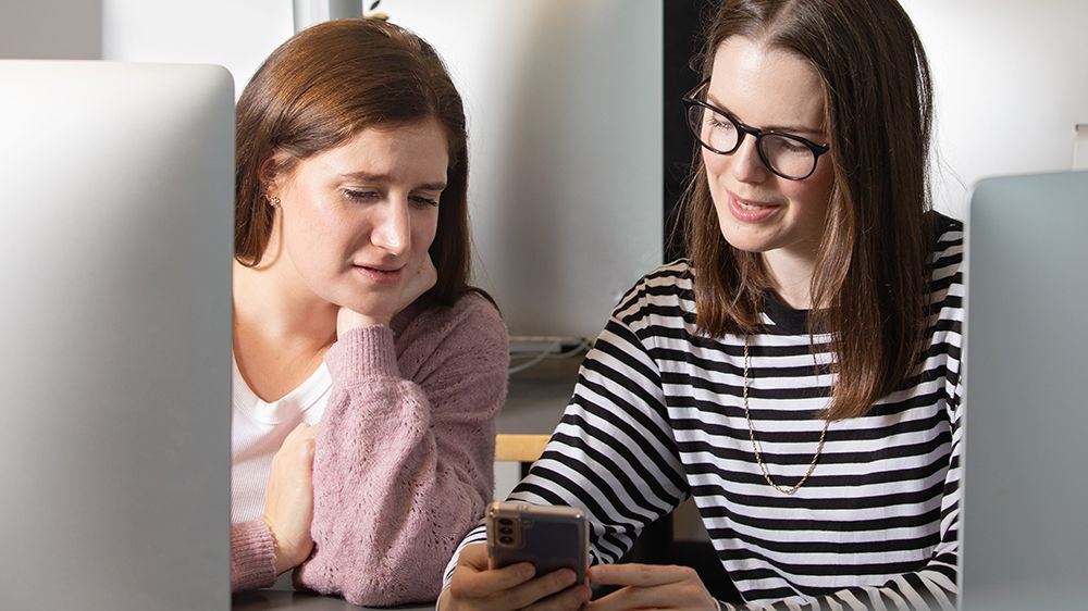 To unge kvinner ser på en smarttelefon. Fotografi.