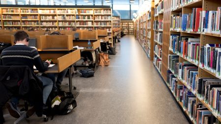 Studenter på lesesal med boksamling og linoleumsgulv. Foto