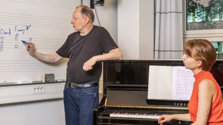 Student and lecturer at blackboard and piano. Photo