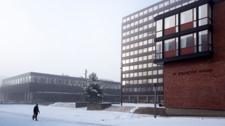 A person crossing a square in front of a building at wintertime, on a foggy and snowy day. Photo