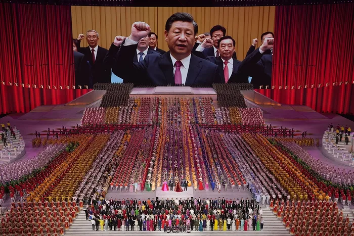Konferanselokale med en publikumsmasse bestående av flere tusen mennesker i festklær som står på gulvet. På en enorm skjermen i bakgrunnen ser vi nærbilde av scenen hvor det står ti-elleve kinesiske menn i sorte dresser med slips, som løfter høyre arm med en knyttneve.