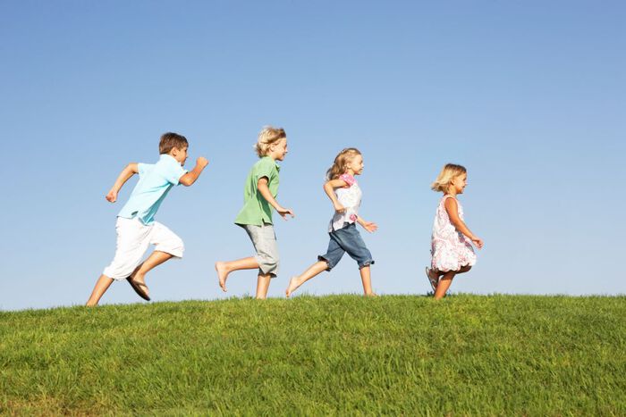fire barn løper etter hverandre på grønt gress, blå himmel