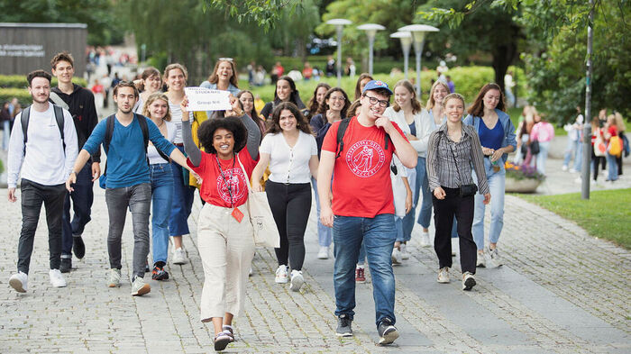 Studenter går i gruppe med faddere i røde t-skjorter som holder et skilt der det står "international students". Foto