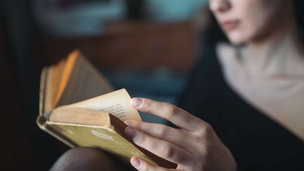 Nærbilde av en kvinne i sort som leser en bok.