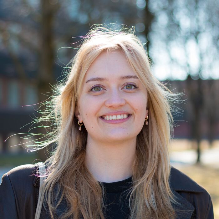 Bildet viser kulturhistorie-studenten Oda smilende foran Blindern, iført en kul jakke, handlenett og band-t-skjorte.