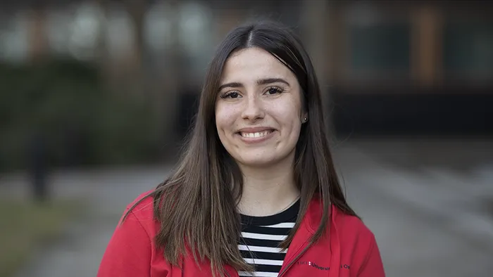 En ung kvinner med mørkt hår, ser rett frem og smiler. Fotografi.